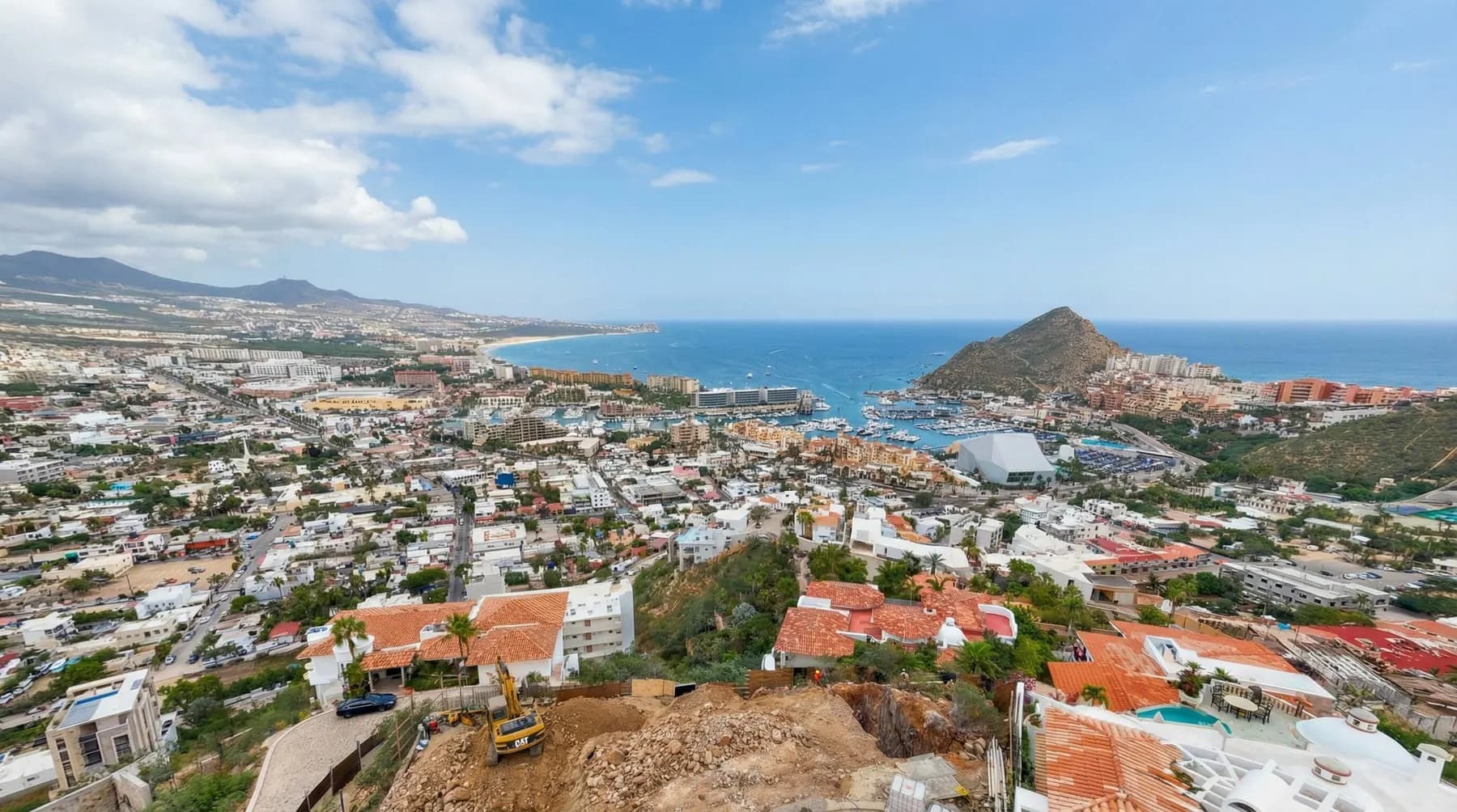 Villa del León under construction in Pedregal, Cabo San Lucas — CAT on the hillside, marina beyond